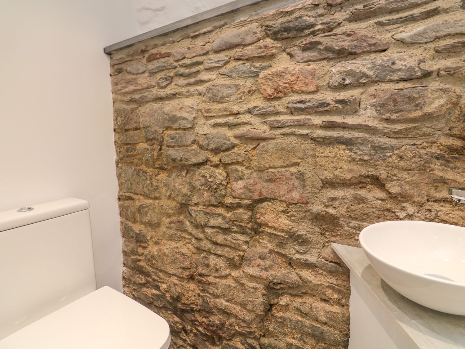 Un baño con pared de piedra, inodoro y lavabo.