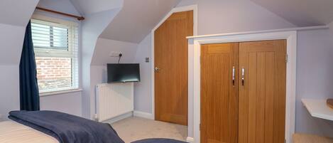 A bedroom with two beds, a wooden wardrobe, a television, and a window with blinds.