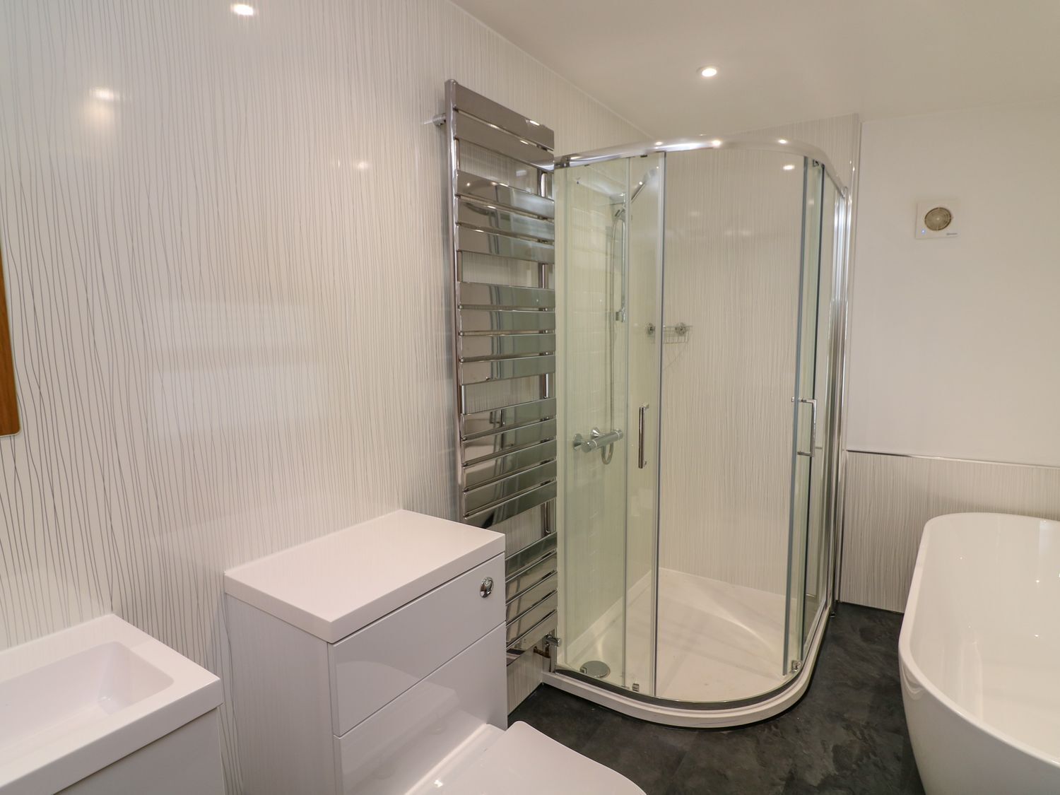 A modern bathroom with a glass-enclosed shower, a white vanity, and a bathtub.
