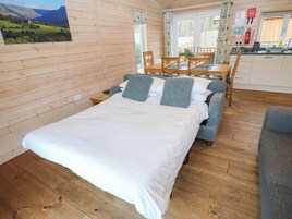Una habitación acogedora con una cama de madera, una mesa de comedor con sillas y una zona de cocina con fregadero y armarios.