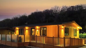 Une cabane en bois dotée d’une terrasse, entourée d’arbres, au crépuscule.