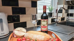 A kitchen counter with a loaf of bread, a bottle of wine, a glass, and a wooden tray with tomatoes. - Sail Lodge (Scarborough)
