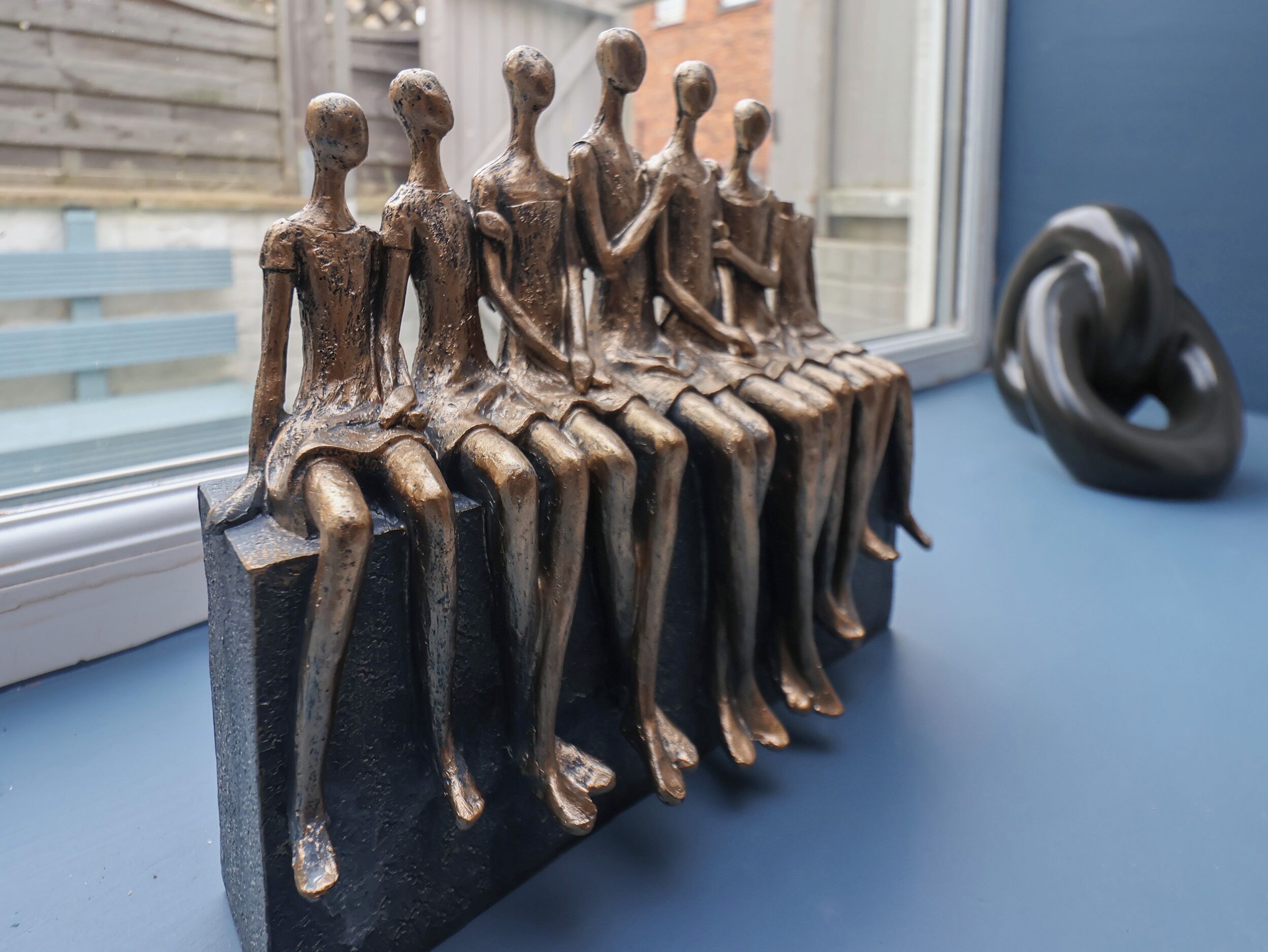 Una escultura de figuras sentadas sobre un pedestal negro junto a una ventana.