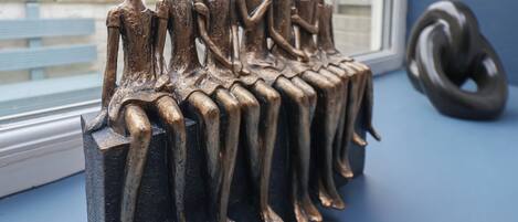 Una escultura de figuras sentadas sobre un pedestal negro junto a una ventana.