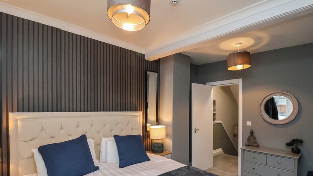 A hotel room with a large bed, a nightstand, a dresser, a mirror, and a door leading to a staircase. - Sail Lodge (Scarborough)