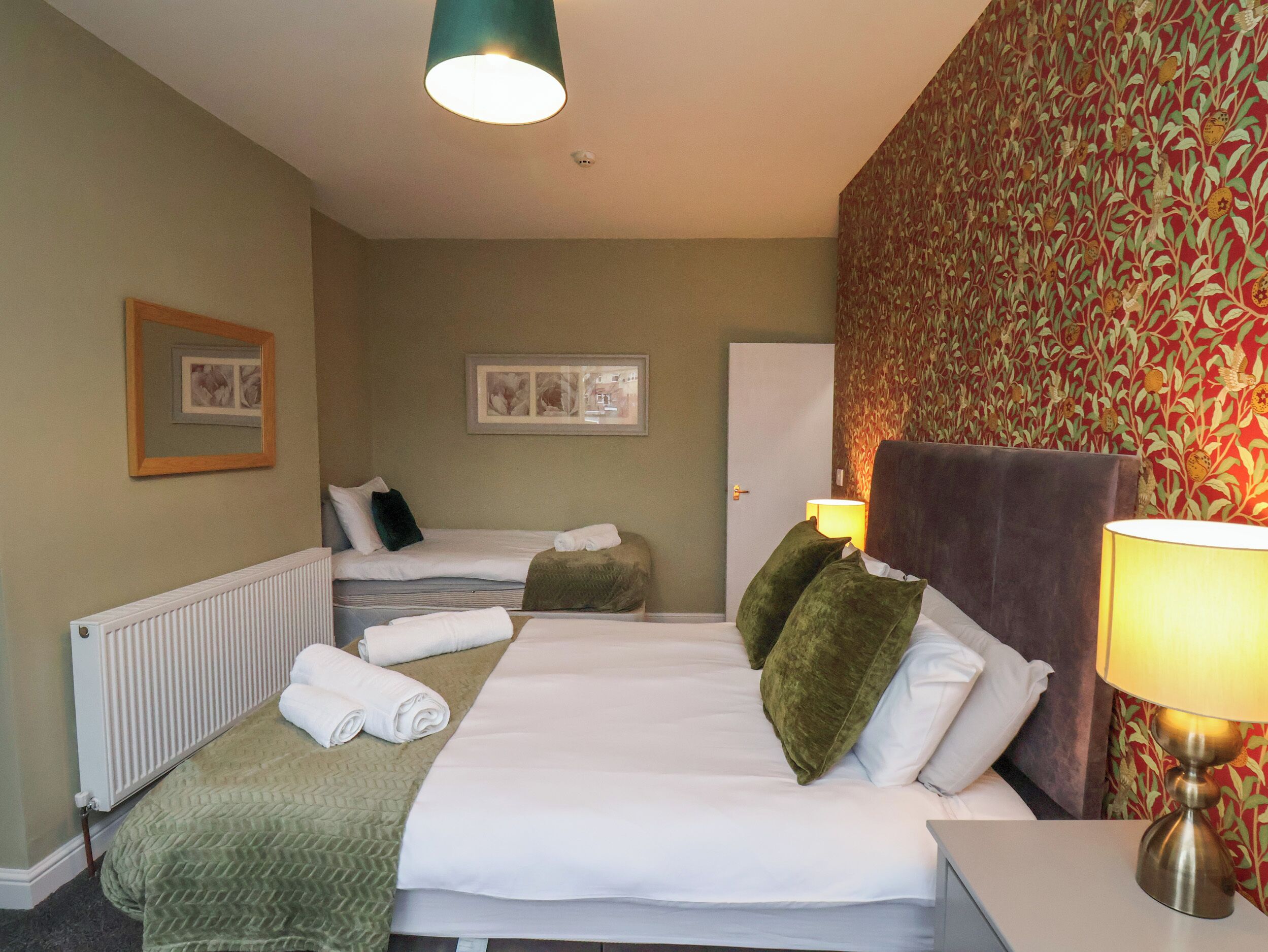 A hotel room with two beds, a radiator, a framed picture, and a patterned wallpaper.