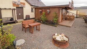 A rustic building with a wooden exterior, a bench, a table, and a fire pit. - Apache Falls Lodge (Limavady)
