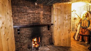 A rustic room with a brick fireplace, wooden walls, and a wooden floor. - Apache Falls Lodge (Limavady)