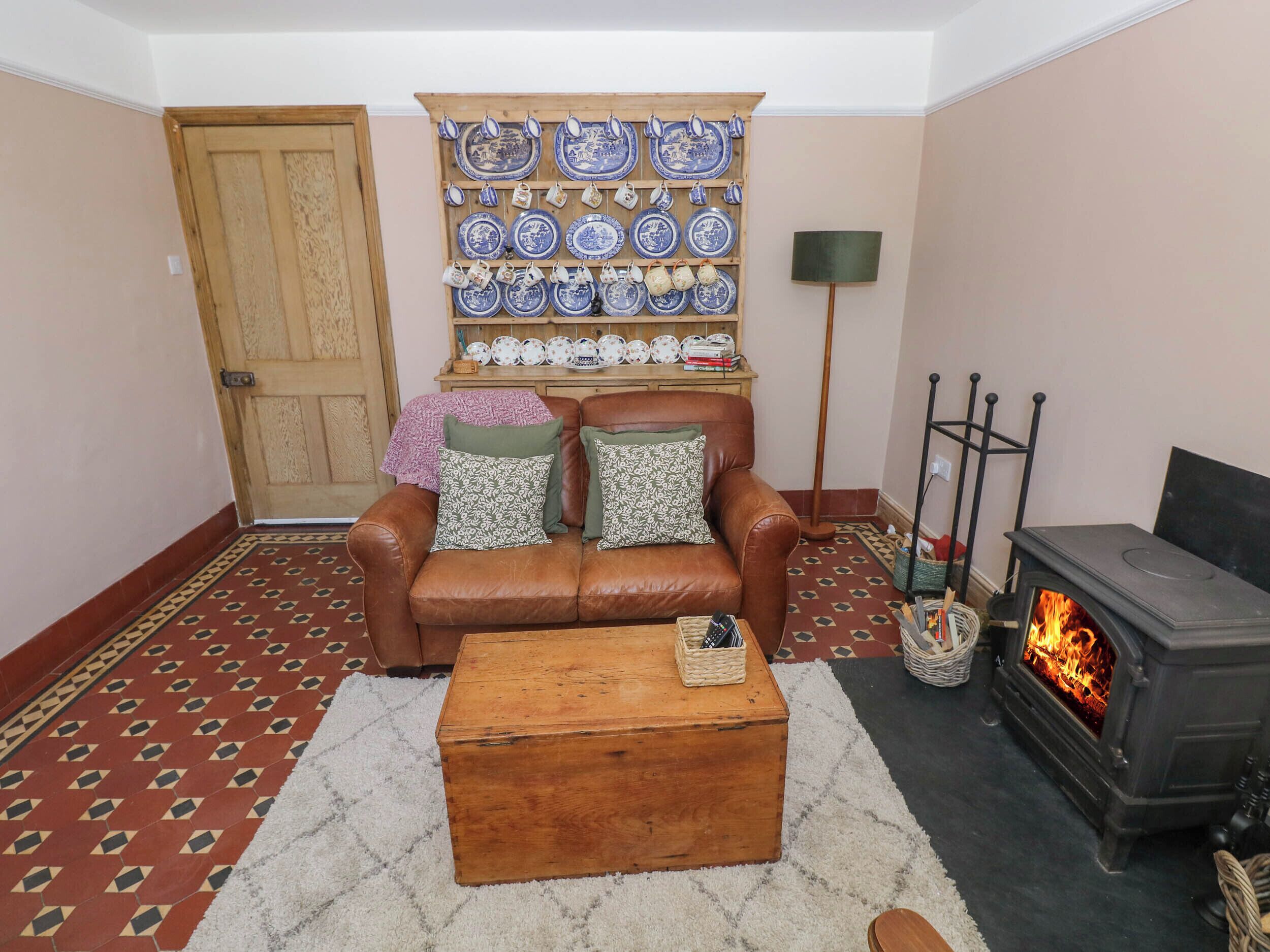 A cozy living room with a brown leather sofa, a wooden coffee table, a fireplace, and a wall-mounted display of blue and white plates.
