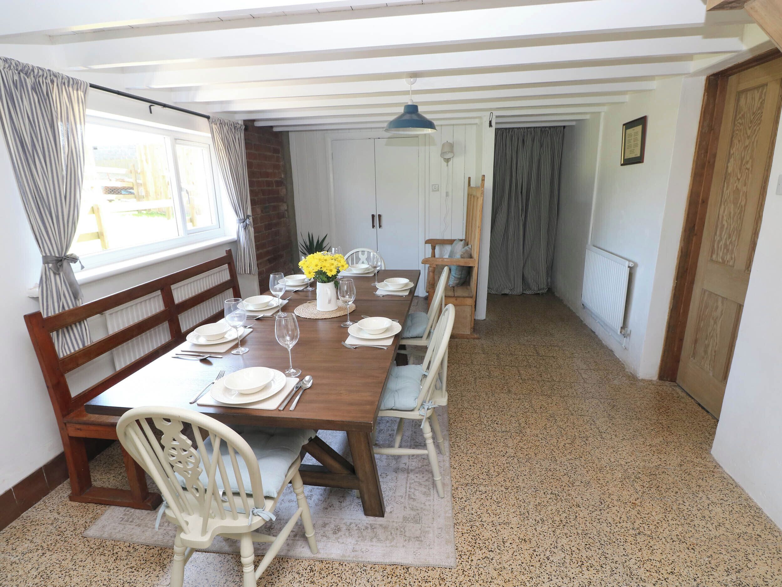 A dining area with a wooden table set for four, white chairs, and a vase of yellow flowers.