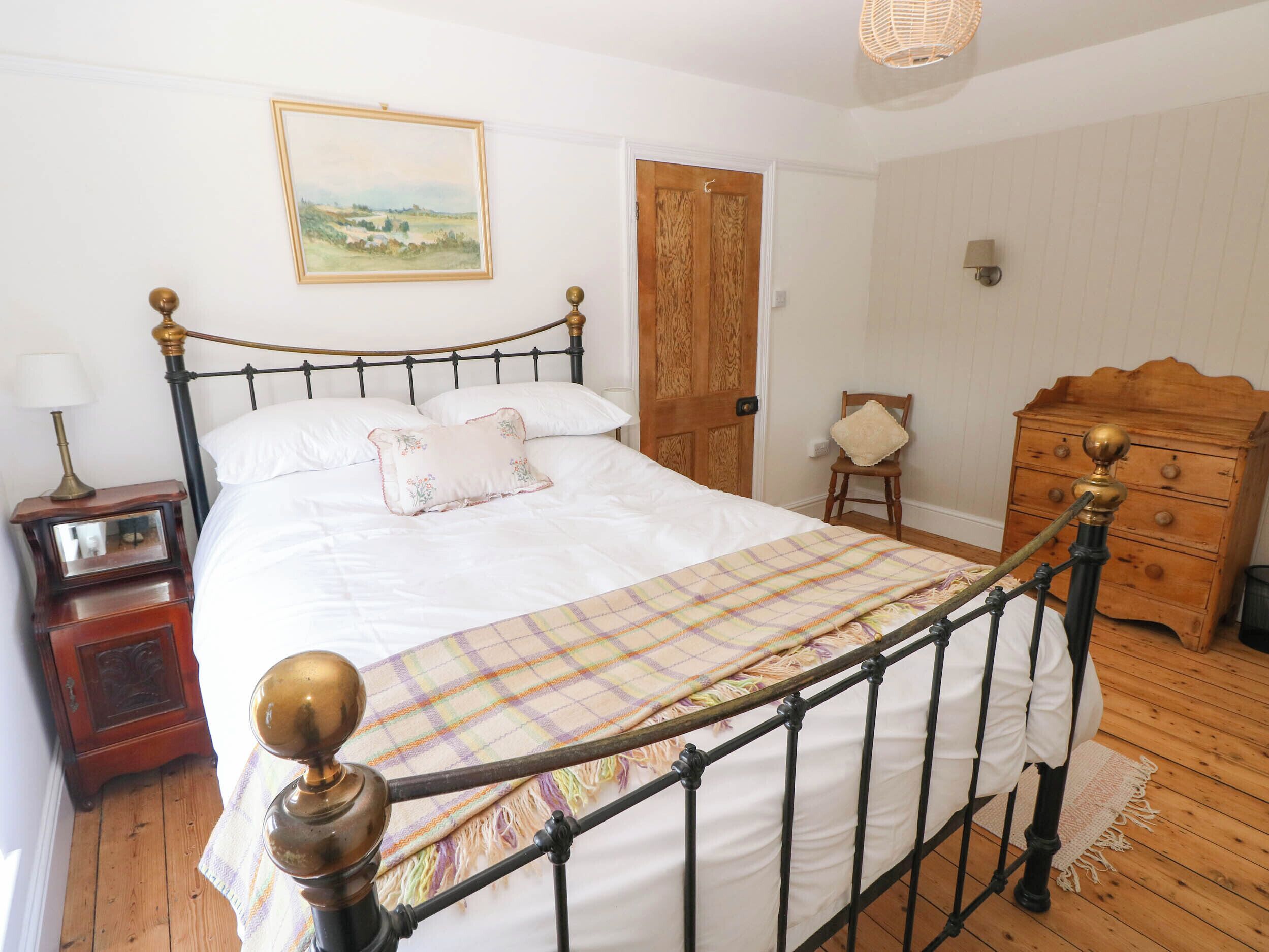 A bedroom with a bed, wooden dresser, nightstand, and a painting on the wall.