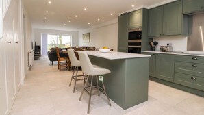 A modern kitchen with a central island, bar stools, and green cabinetry. - Pear Tree Cottage (Preston)