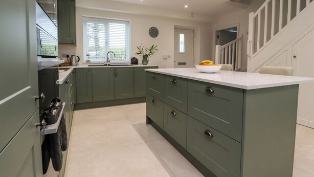 A modern kitchen with green cabinets, a white countertop, and a bowl of fruit on the island. - Pear Tree Cottage (Preston)