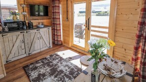 A rustic cabin interior with wooden walls, a kitchen area, a large window, and a view of the outdoors. - Rocky Ridge Cabin (Limavady)