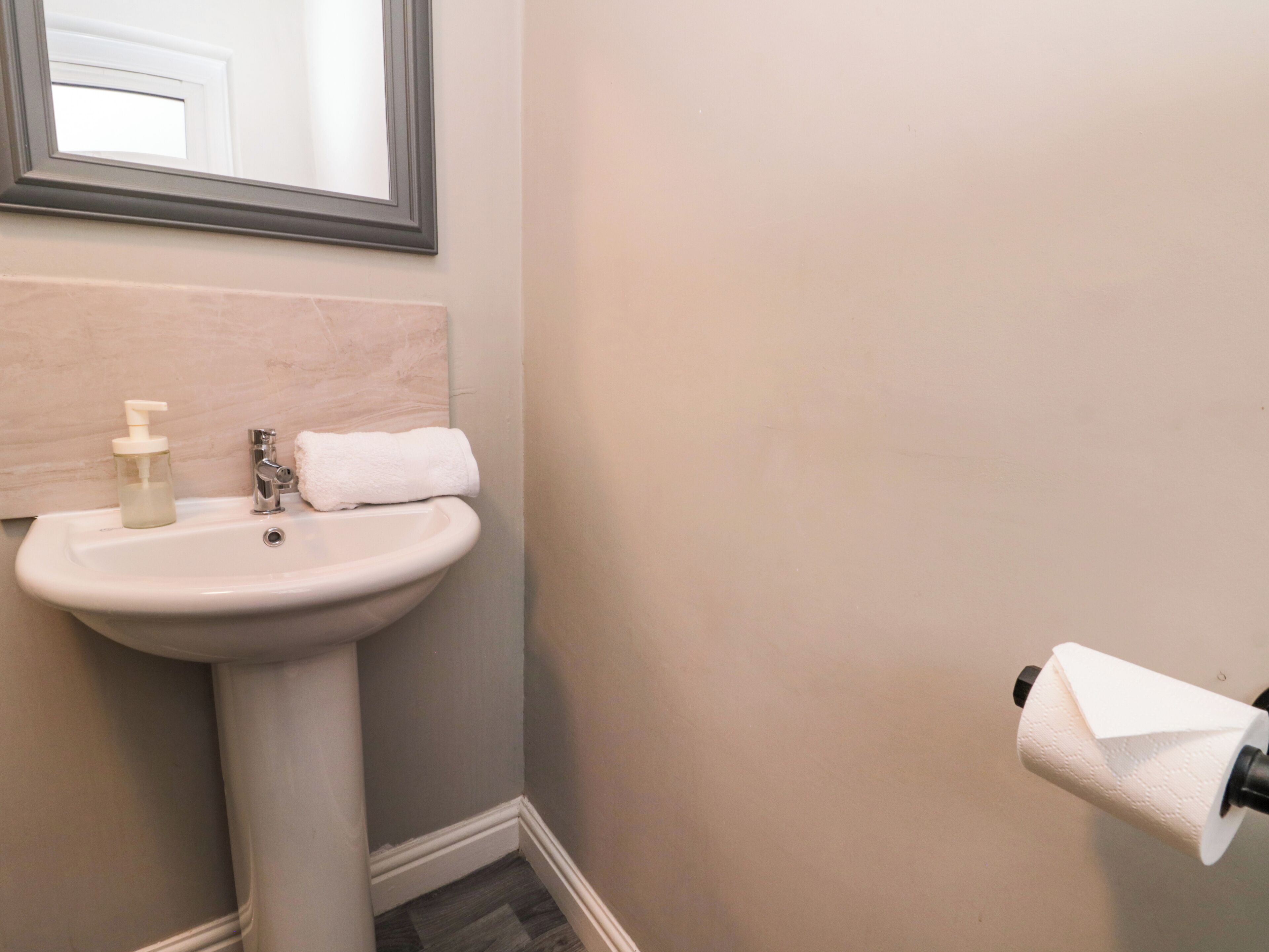 Un baño con lavamanos pedestal, espejo, toalla y soporte para papel higiénico.