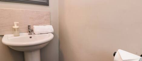 Un baño con lavamanos pedestal, espejo, toalla y soporte para papel higiénico.