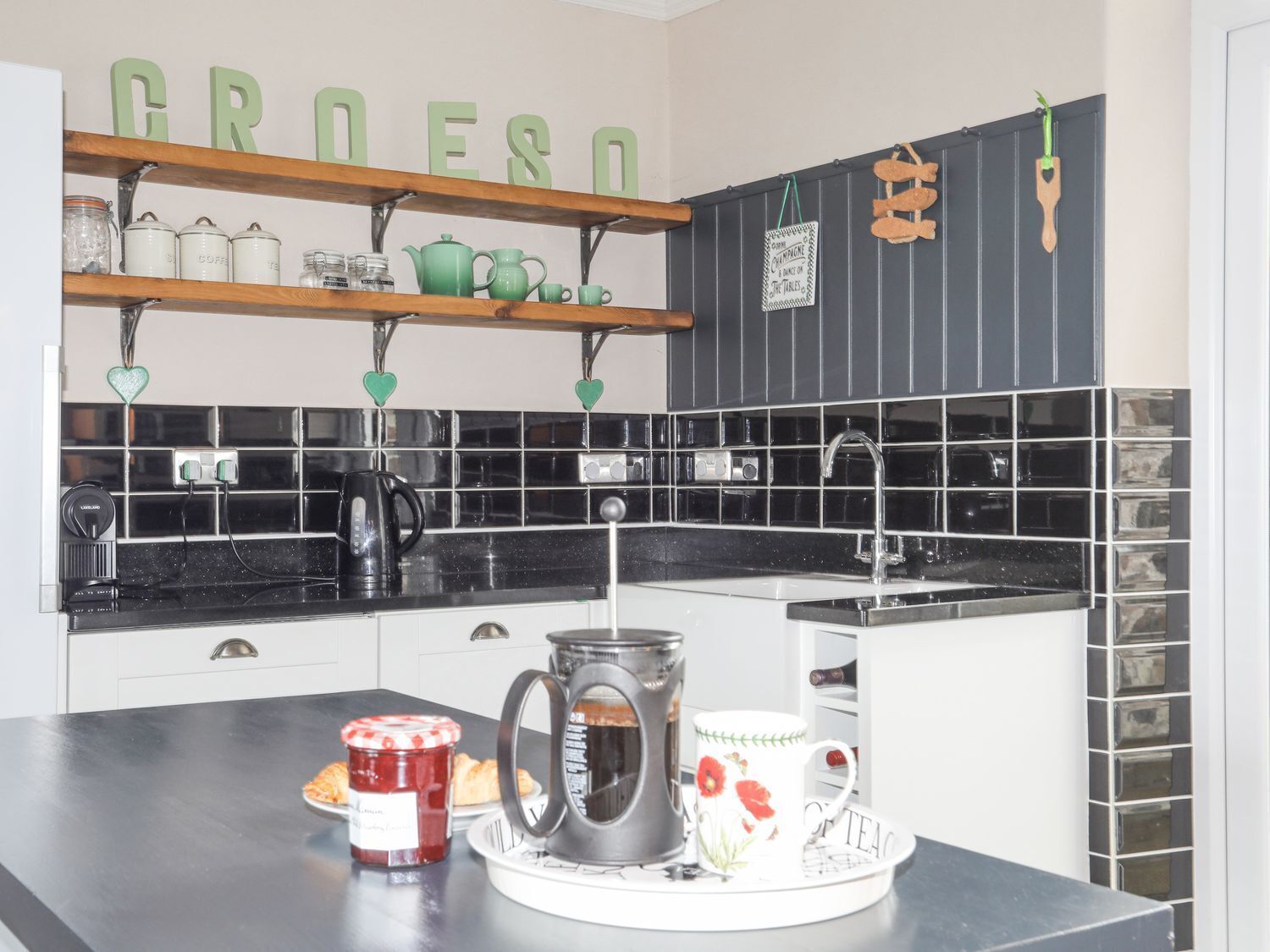 Een keuken met zwart-wit betegeling, een koffiezetapparaat, een waterkoker en een pot jam op het aanrecht.