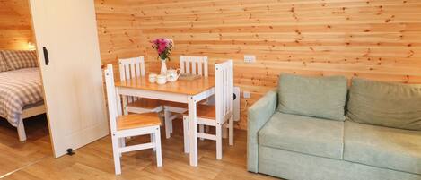 Une pièce chaleureuse avec un plafond en bois, une table à manger avec des chaises, un canapé vert et un lit avec une literie à carreaux.