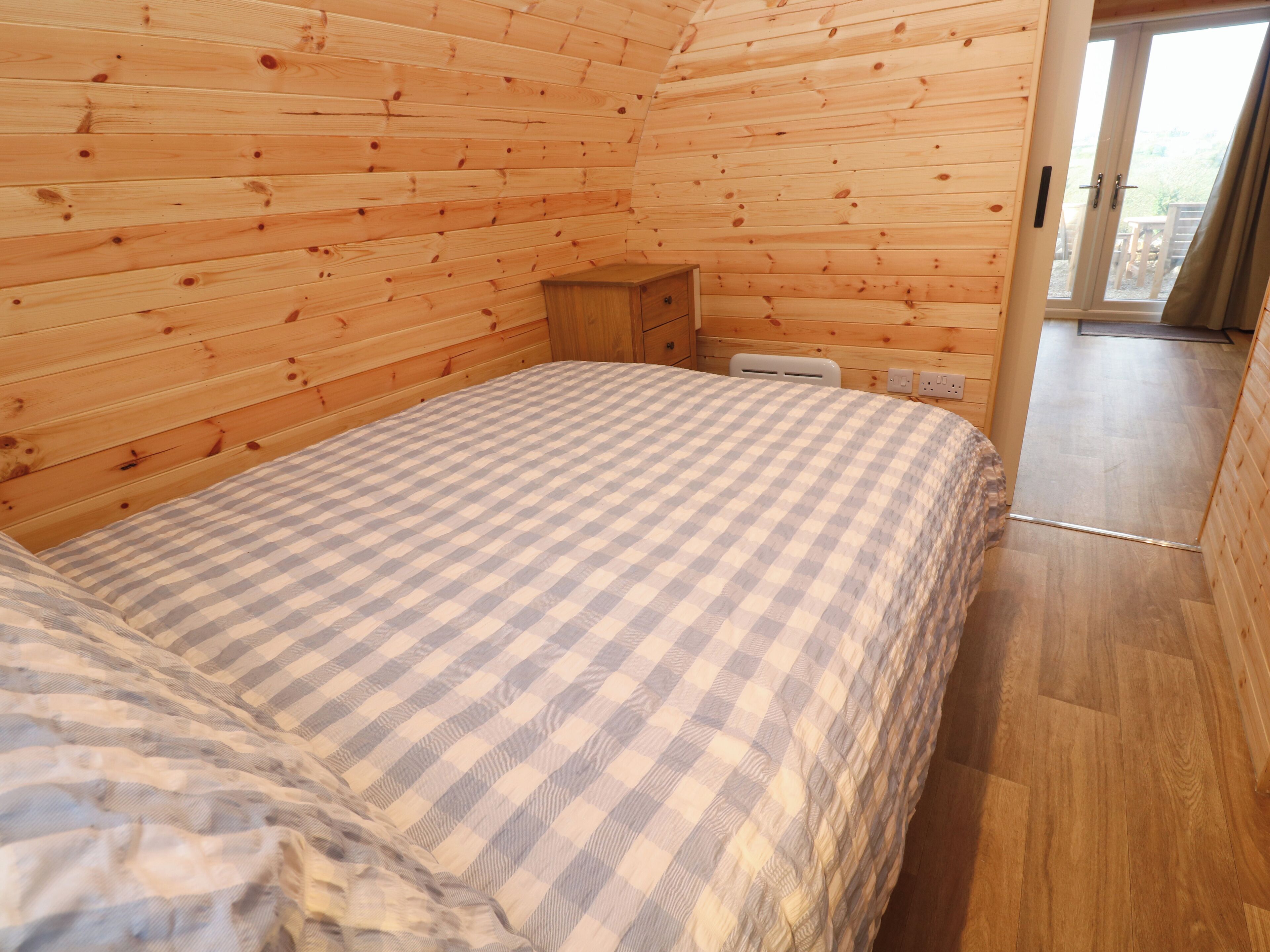 A cozy wooden cabin room with a checkered bedspread, a wooden nightstand, and a sliding glass door leading to an outdoor area.