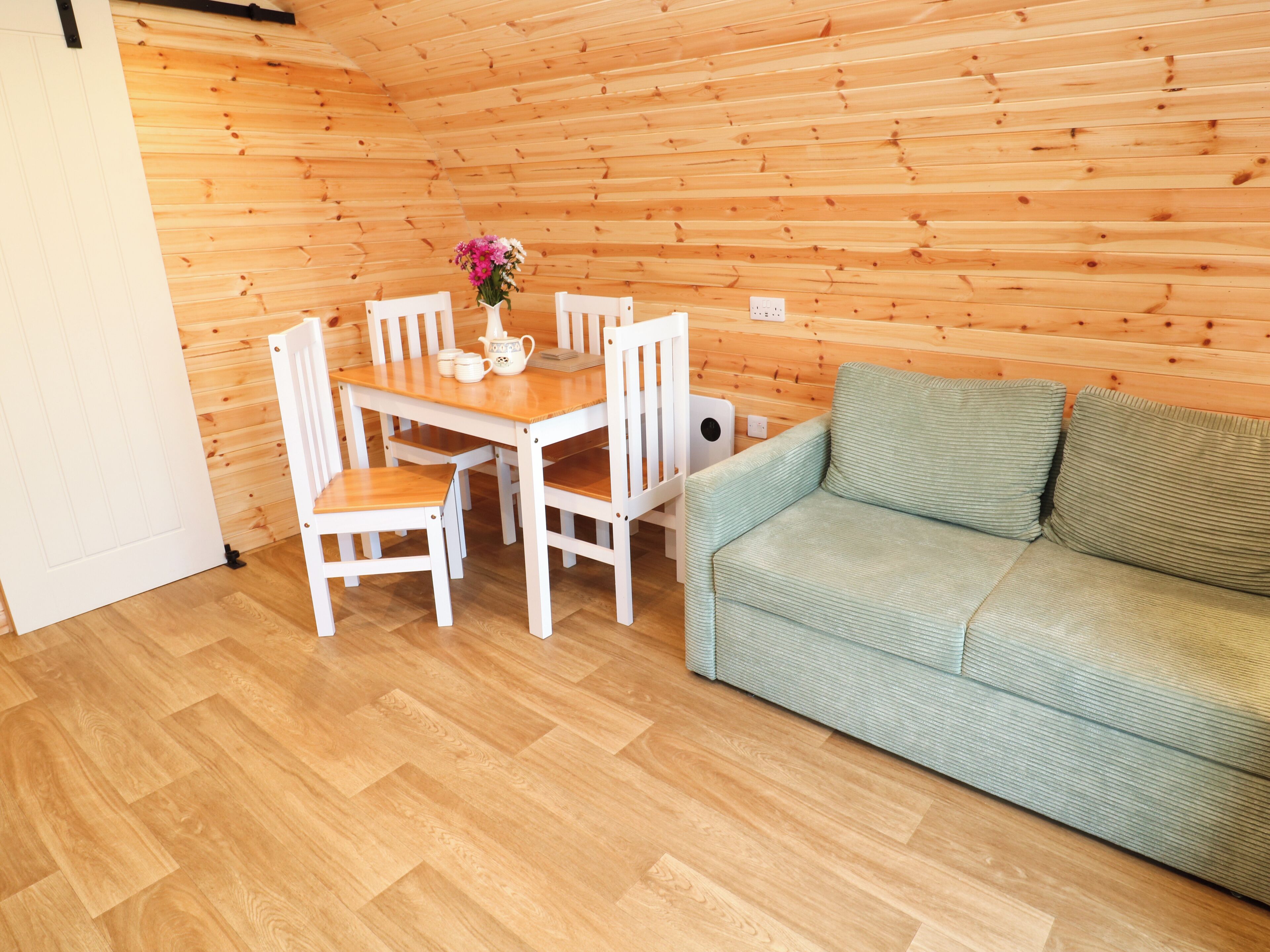 Een houten interieur met een eettafel, stoelen, een bank en een bloevas.