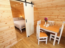 Un interior de madera con una cama, una mesa con sillas y un armario blanco.