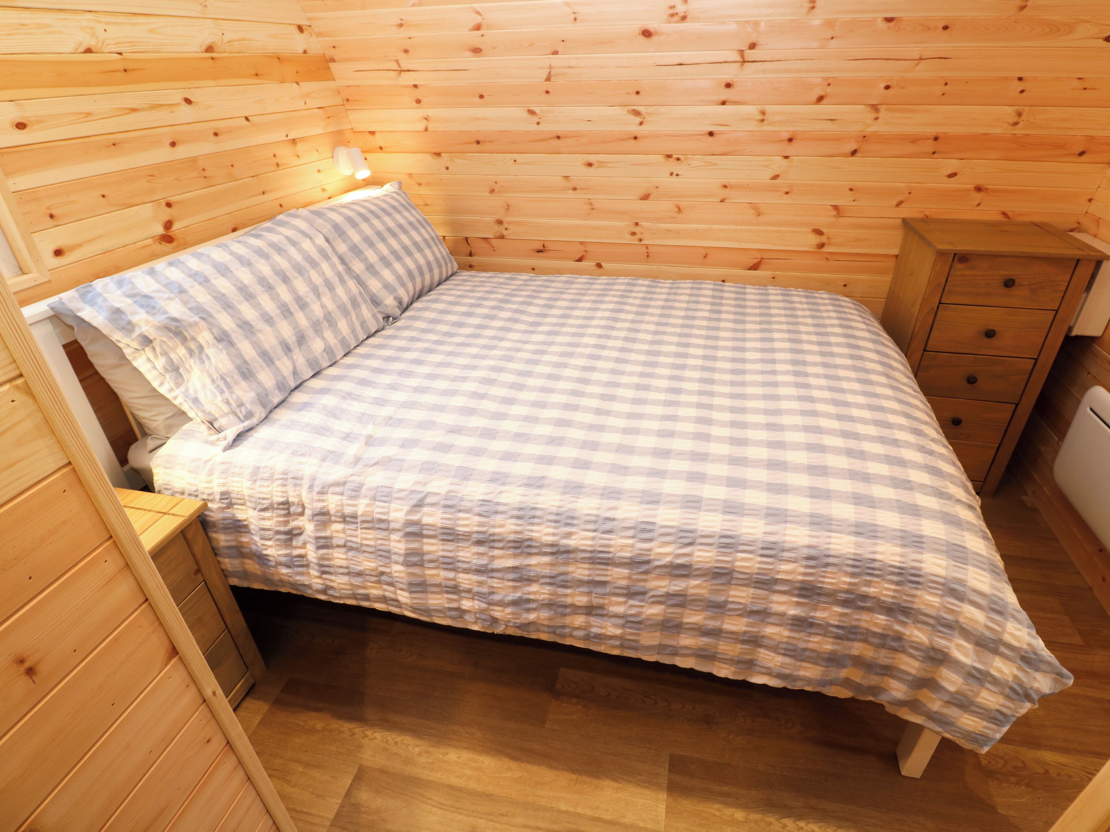 A wooden-paneled room with a bed, a nightstand, and a small wooden cabinet.