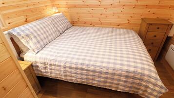 Ein Zimmer mit Holzwänden, einem Bett, einem Nachttisch und einem kleinen Holzschrank.