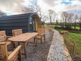 A cozy outdoor seating area with wooden furniture and a gravel path leading to a rustic wooden gate.
