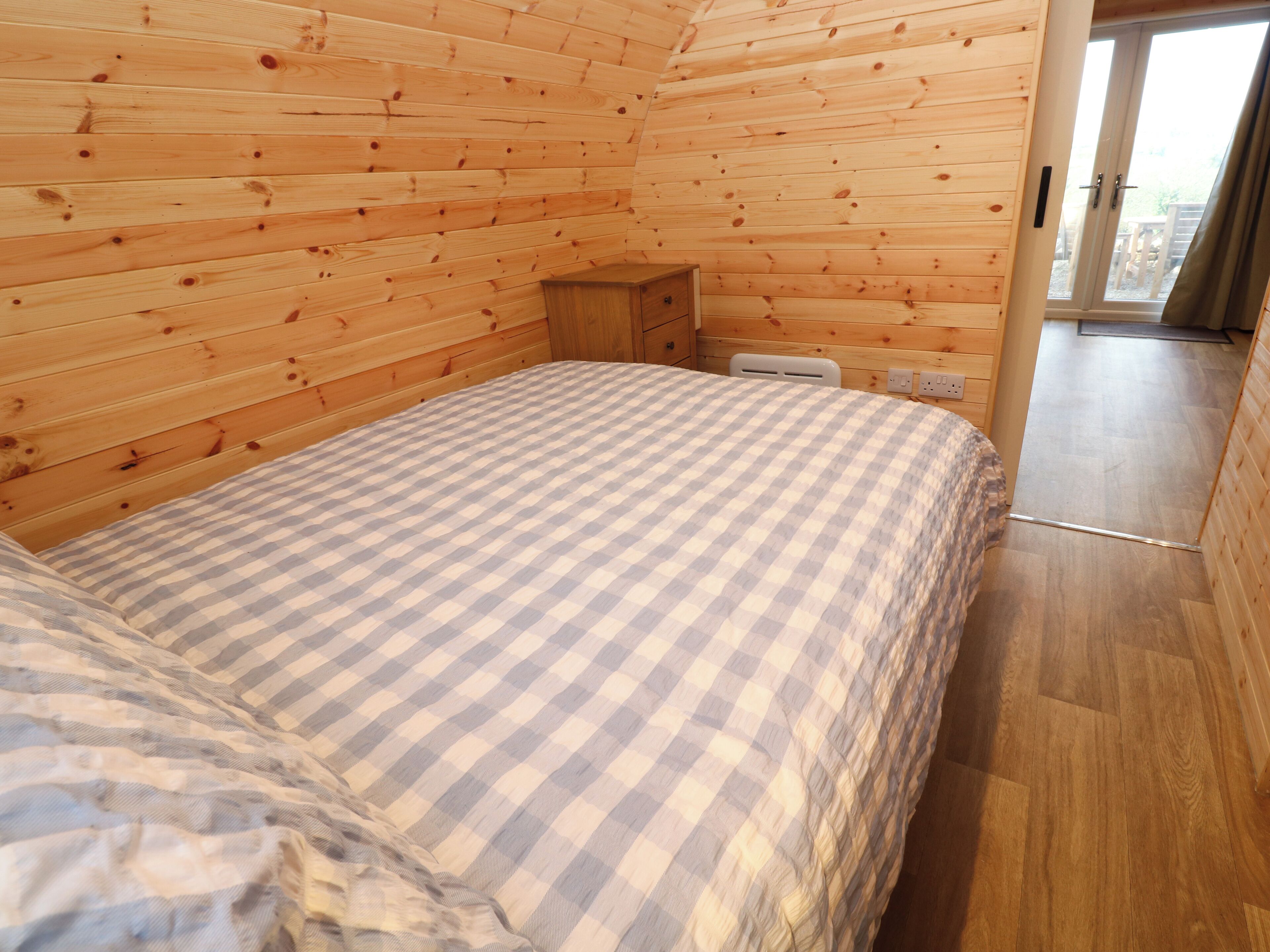 A cozy wooden cabin room with a checkered bedspread, a wooden nightstand, and a sliding glass door leading to an outdoor area.
