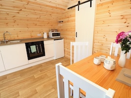 A modern kitchen with wooden walls, a wooden dining table, white chairs, a white cabinet, a microwave, a sink, and a coffee maker.