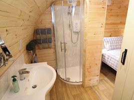 Una cabaña de madera pequeña con ducha, lavamanos y cama.