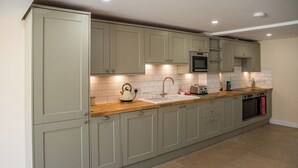 Una cocina con armarios verde claro, encimera de madera, microondas de acero inoxidable y un lavabo.