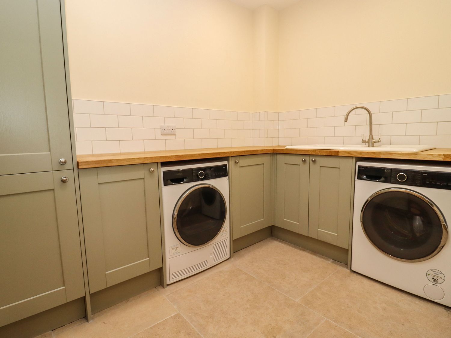 A compact laundry room with two front-loading washing machines, a sink, and light-colored cabinets.