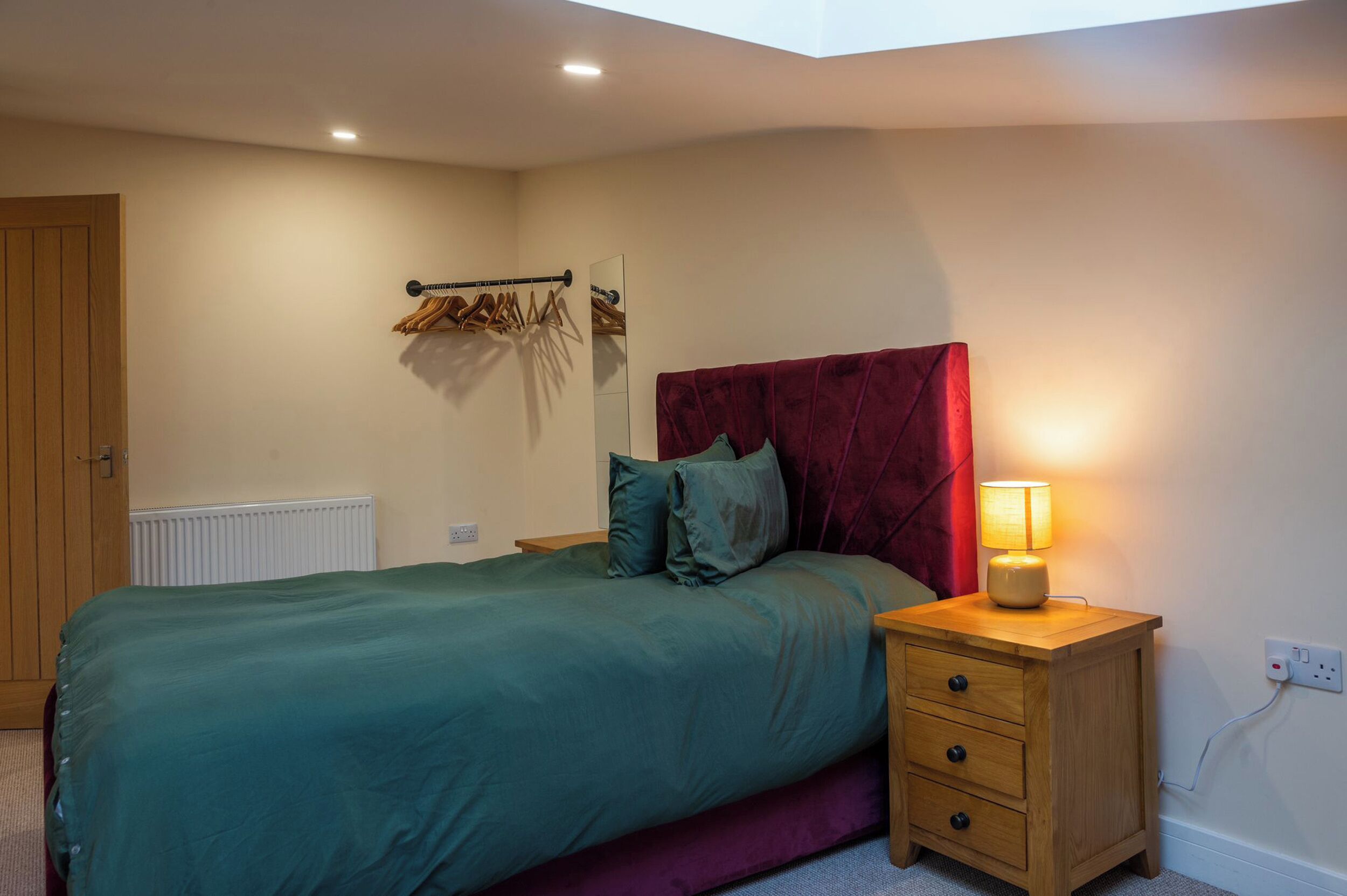 Ein Schlafzimmer mit einem Bett, einem Nachttisch, einer Lampe, einem Heizkörper und einer Holztür.
