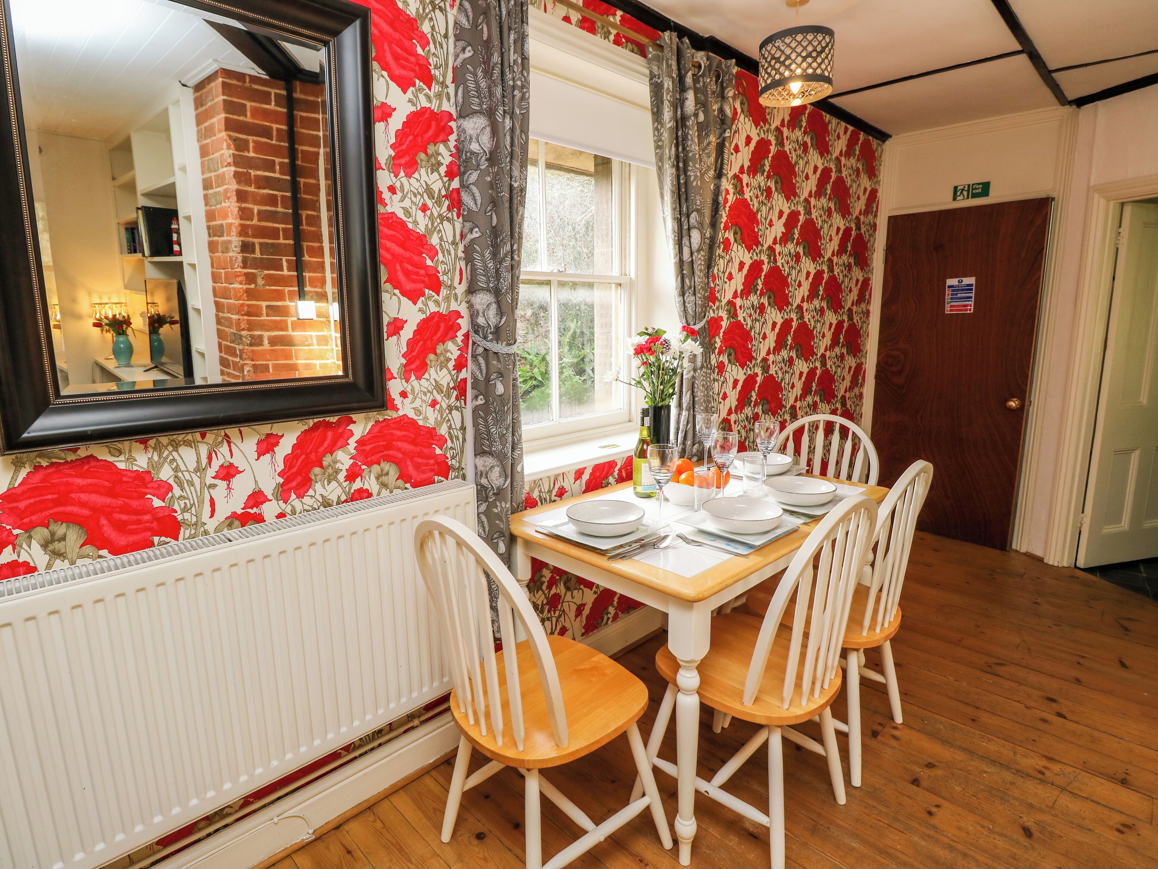 A dining area with a table set for four, white chairs, a brick fireplace, and floral wallpaper.