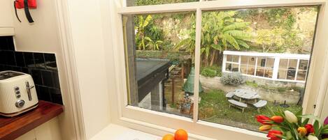 A kitchen with a white countertop, a toaster, a window with a view of a garden, and a vase with flowers on the windowsill.