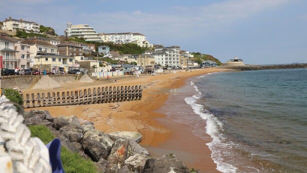 Une ville côtière dotée d’une plage de sable, d’une promenade et de bâtiments qui bordent le littoral.