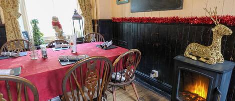 Un comedor acogedor con mantel rojo, sillas de madera, chimenea con un reno decorativo y una pizarra con escritura en la pared.