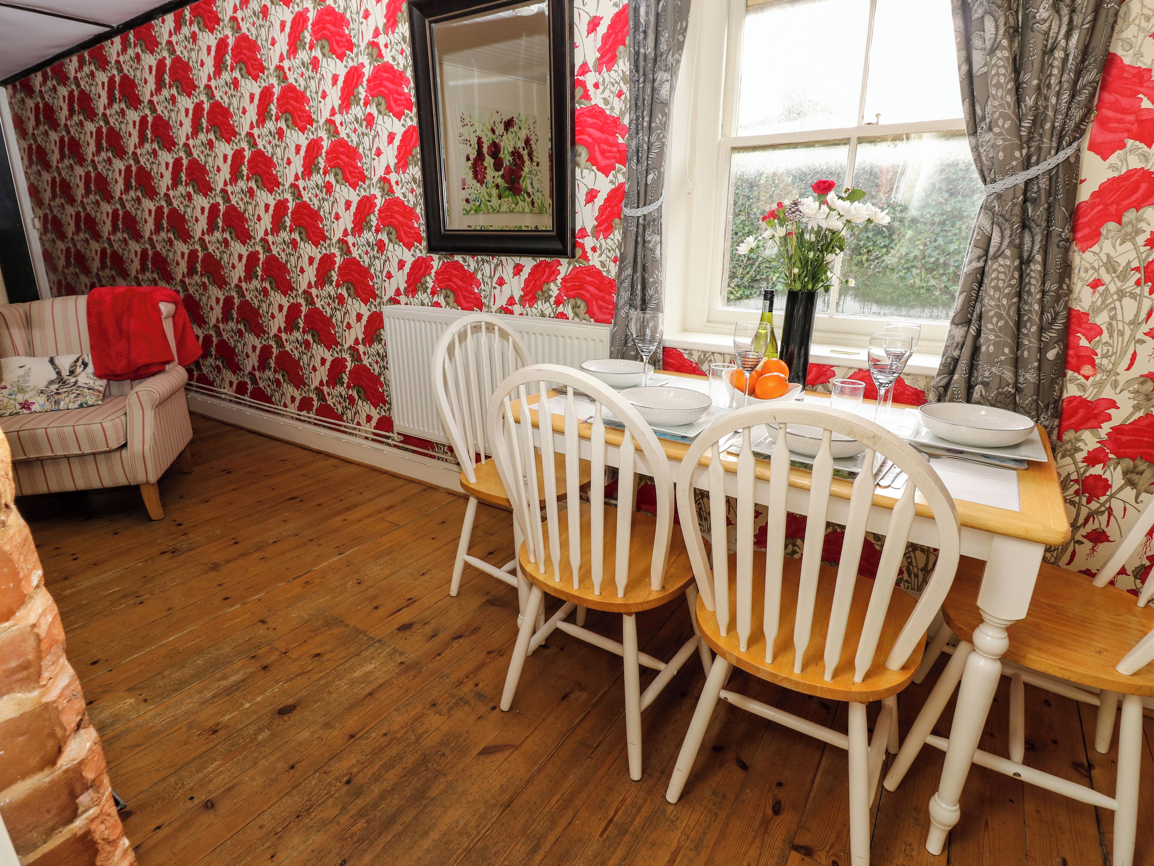 Un coin repas avec une table en bois, des chaises blanches et un papier peint à motifs floraux.