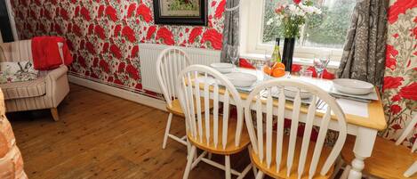 Un coin repas avec une table en bois, des chaises blanches et un papier peint à motifs floraux.