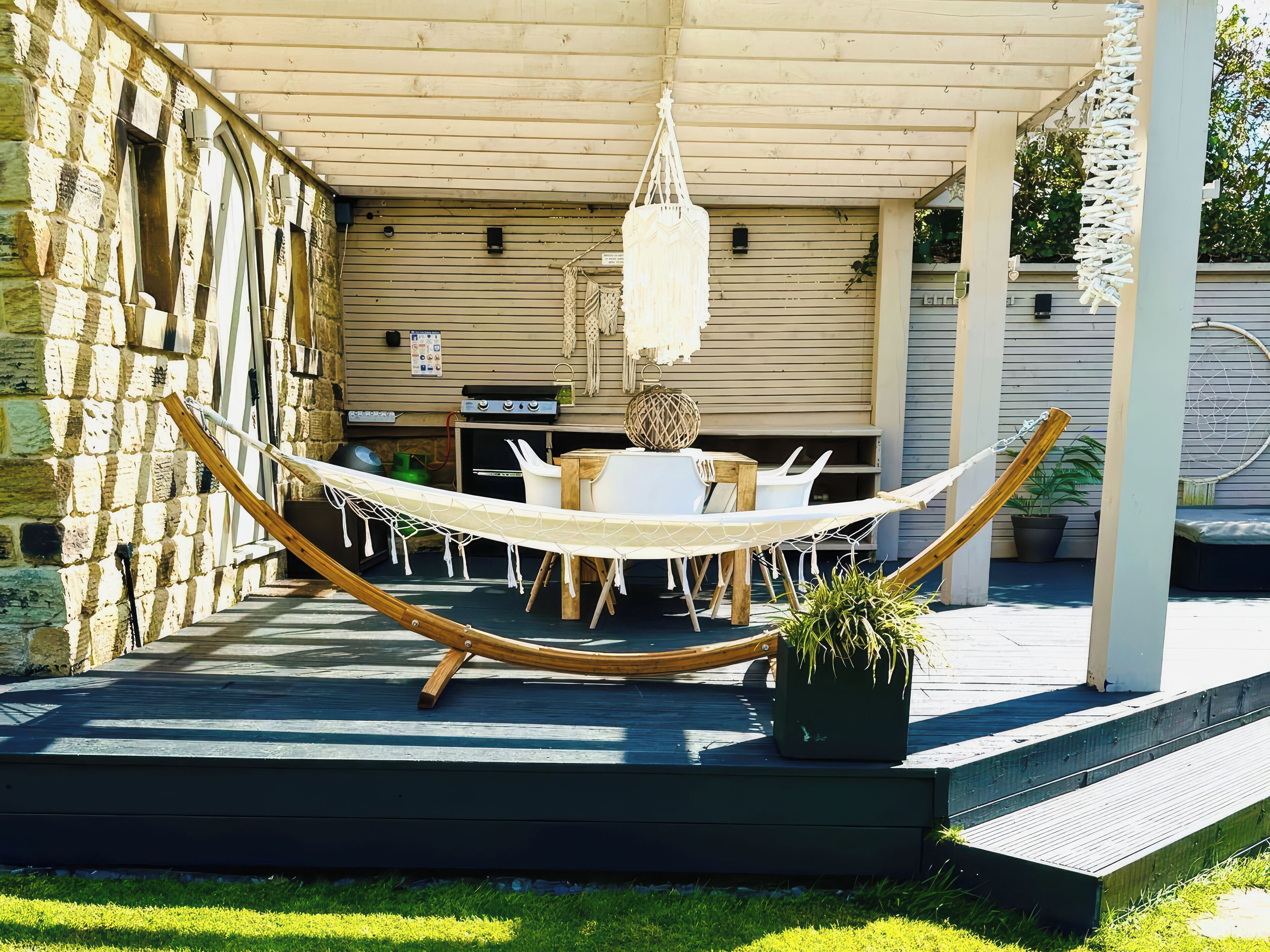 Eine überdachte Terrasse mit Hängematte, Sitzgelegenheiten im Freien und Grillplatz.