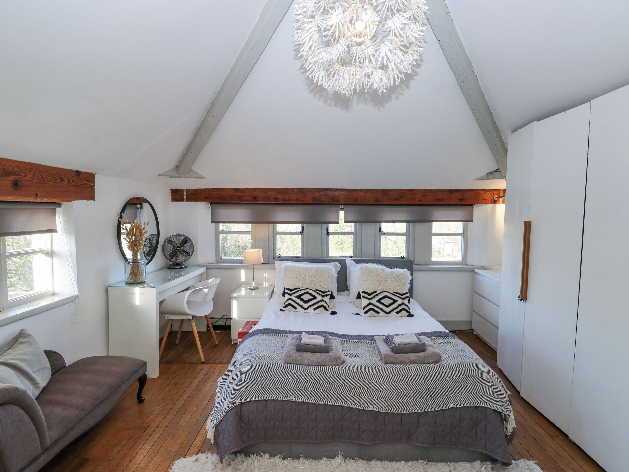 Une chambre à coucher comprenant un lit, des tables de chevet, un bureau, une chaise, un canapé et un luminaire au plafond.