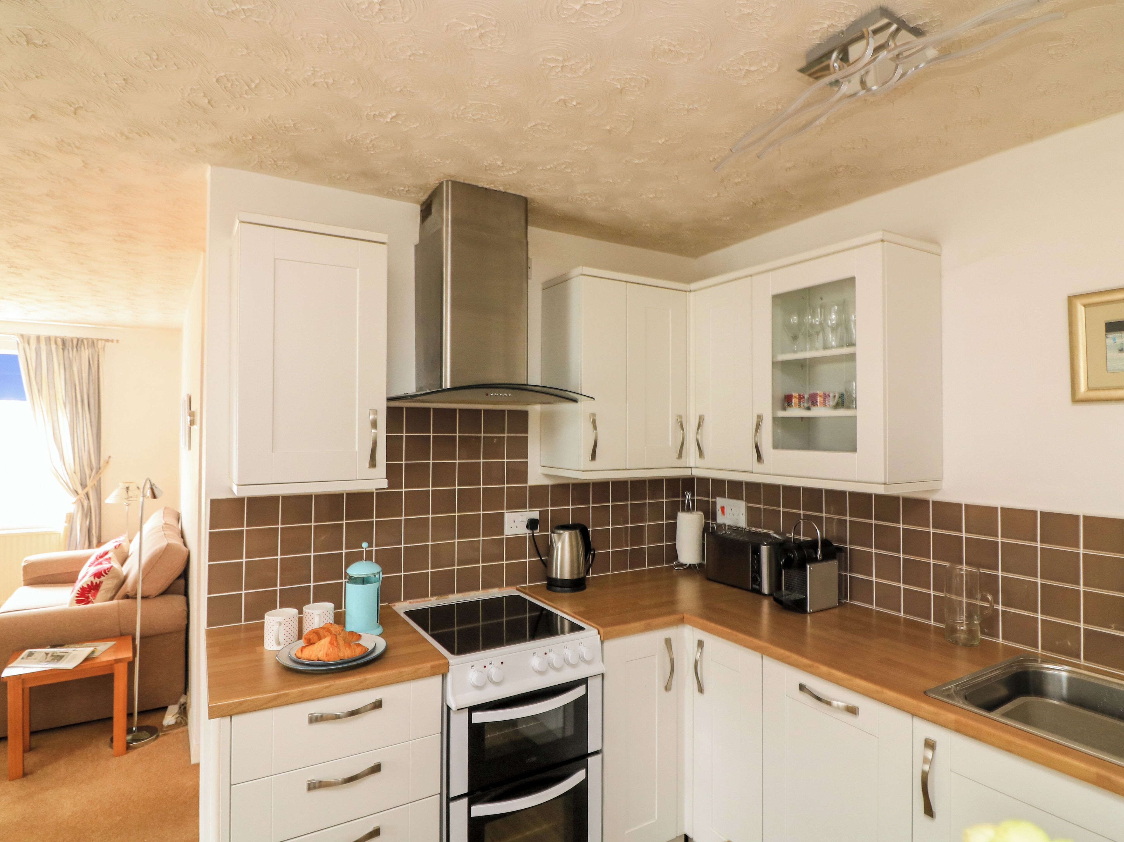 A modern kitchen with white cabinets, a stainless steel range hood, and a wooden countertop.