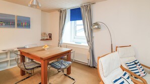 A cozy room with a wooden dining table, two striped chairs, a white sofa with striped pillows, a floor lamp, and a window with curtains. - Sunnyhaven (Dartmouth)