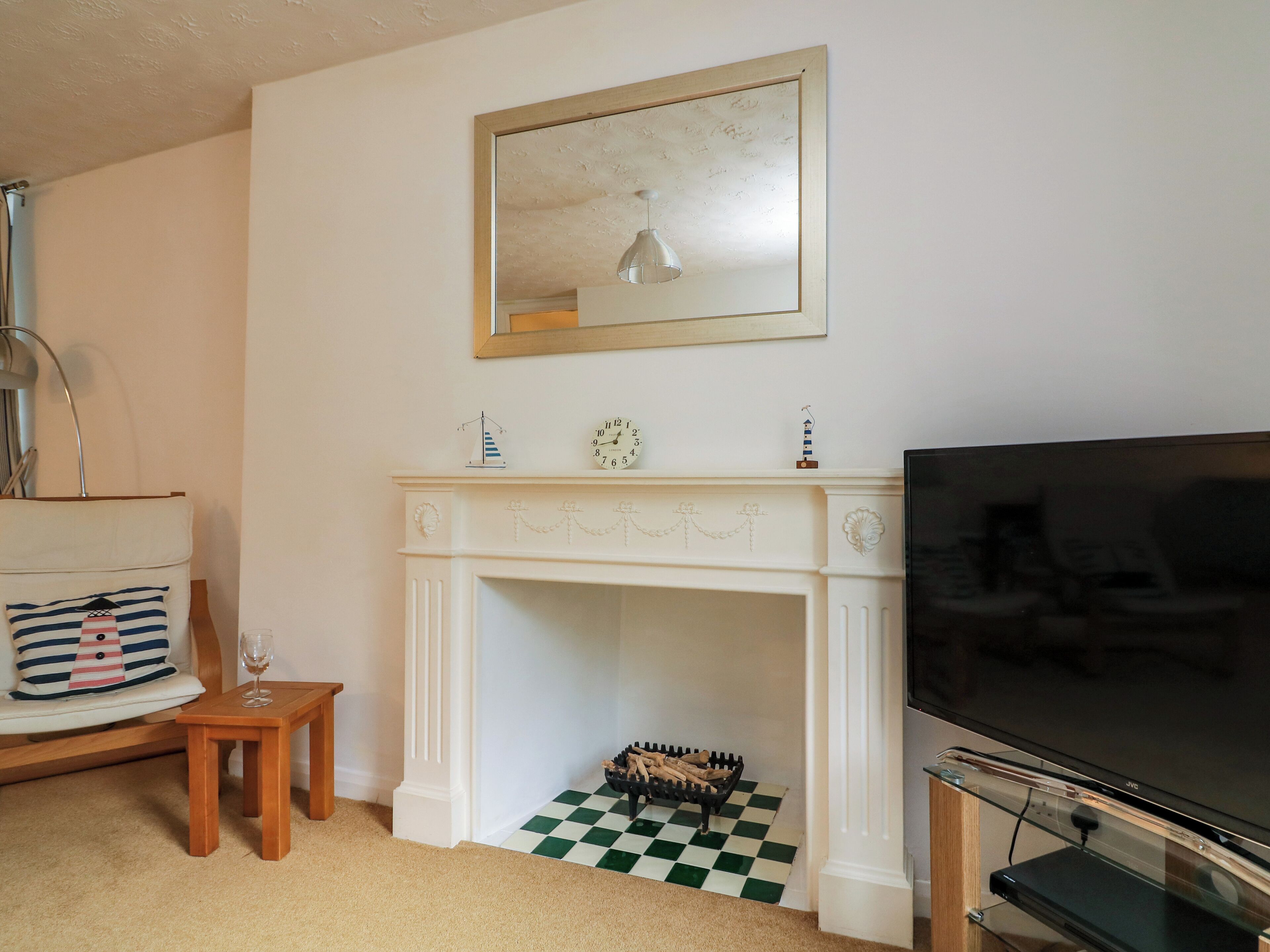 A living room with a white fireplace, a television, and a small table with a glass.