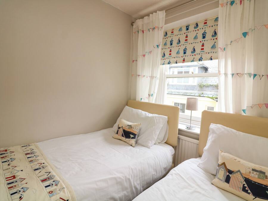 A bedroom with two single beds, a window with curtains, and a view of the outside.