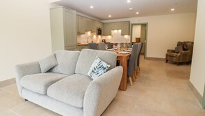 A living room with a grey sofa, a dining table with chairs, and a kitchen in the background. - Bears Court Barn 3 (Cheltenham)