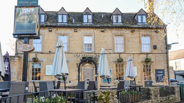 A traditional stone building with a sign for the Old Manse Hotel. There are outdoor seating areas with umbrellas and a stone wall in front. - Bears Court Barn 3 (Cheltenham)