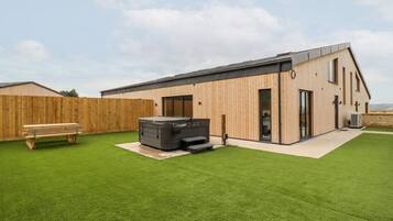 Un edificio moderno con rivestimento in legno, una vasca idromassaggio e un tavolo da picnic in un giardino erboso.