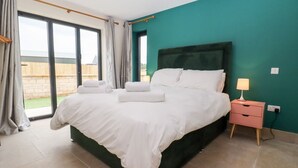 A bedroom with a large bed, a nightstand, and a view through a sliding glass door. - Bears Court Barn 3 (Cheltenham)